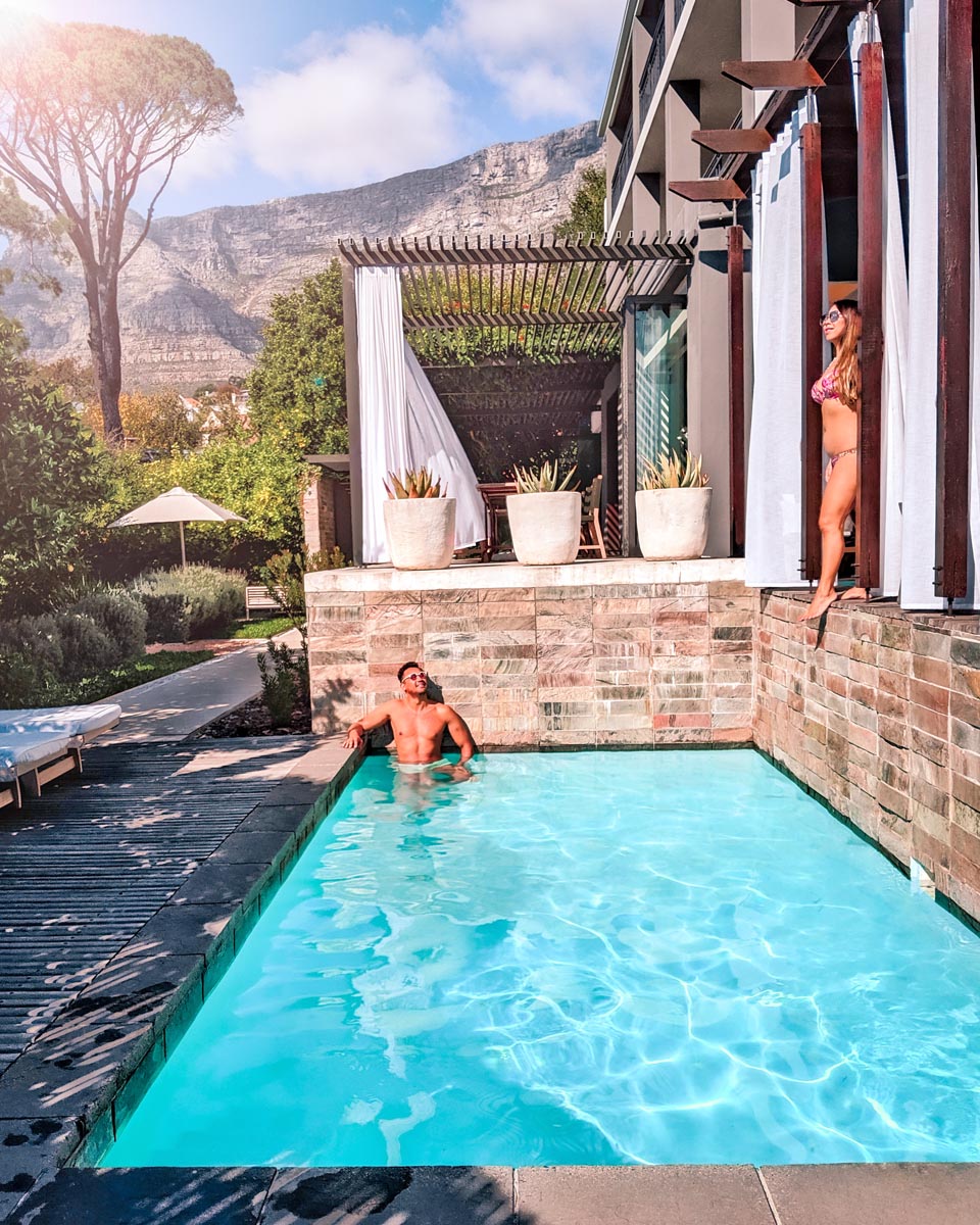 a man in a swimming pool at kensington place boutique hotel in cape town and a woman standing nearby with table mountain in the background