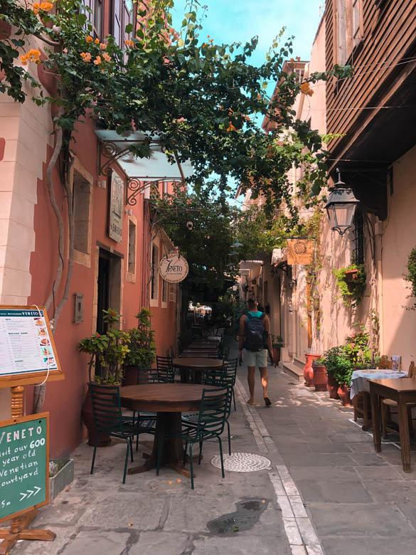 a man walking through a narrow alleyway in rethymno crete with restaurants and cafes 