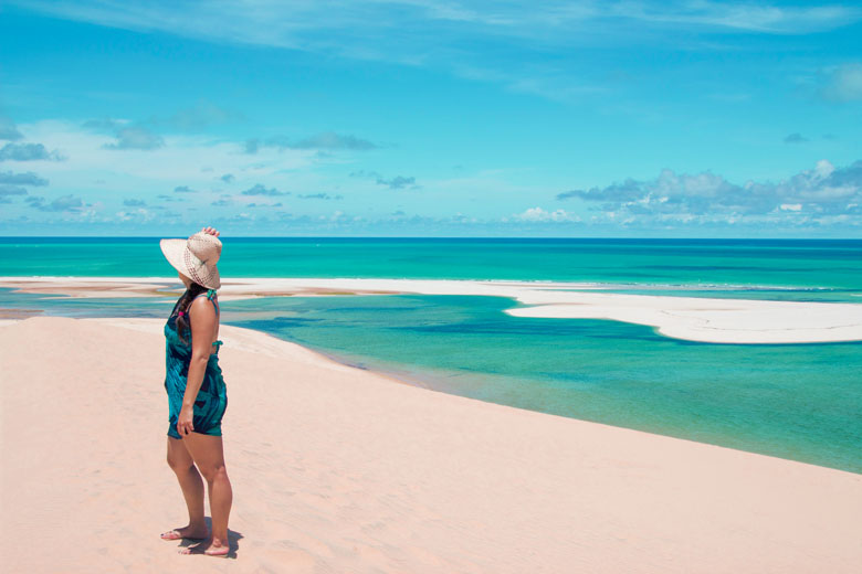 a woman standing on top of a white sand dune on Bazaruto Island overlooking crystal clear blue waters in the distance admiring the views of the Indian Ocean in Mozambique
