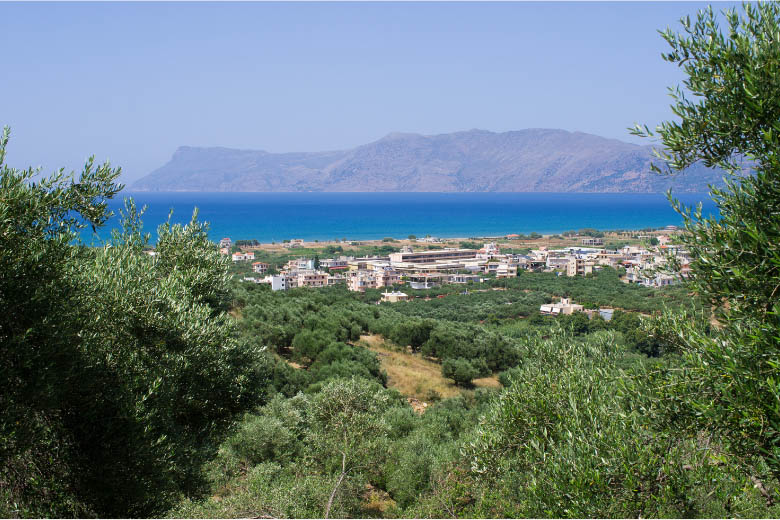 a view of the port city of kissamos in crete with residential buildings, the ocean and mountains in the background