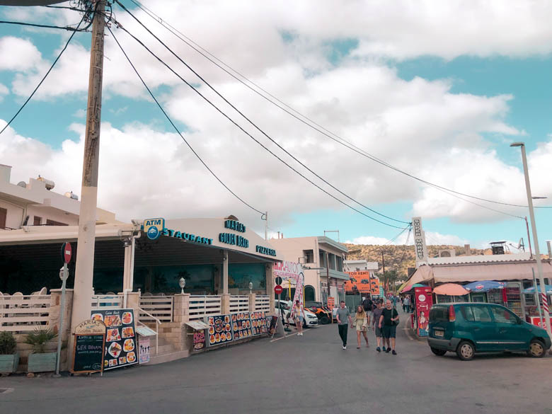 a view of stalis town in crete during the day with restaurants, shops and cafes lining the main road