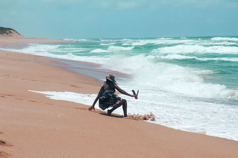 a woman tripping over a fast approaching crashing wave on a stretch of beach in Xai Xai Mozambique