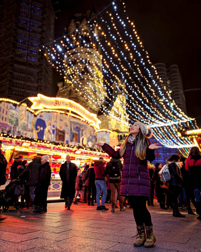 a woman wearing a hat, large coat, scarf, thermal leggings and snow boots at a christmas market in west berlin germany