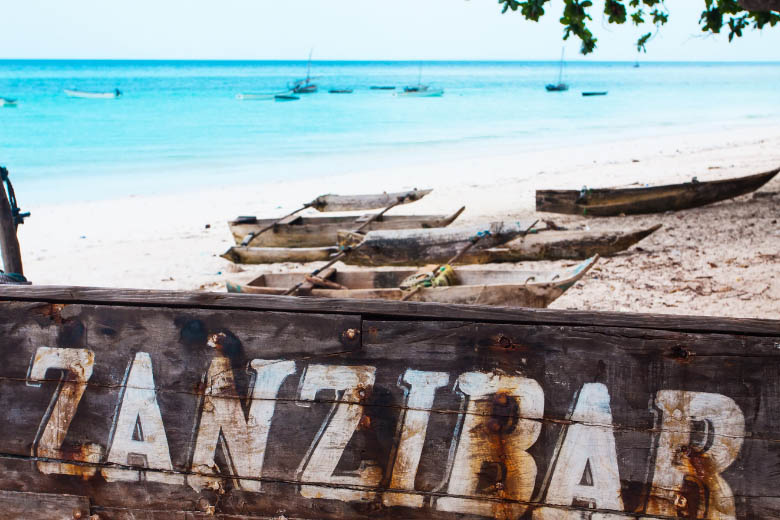 wood boats lying on the beach in zanzibar with turquoise blue ocean in the background