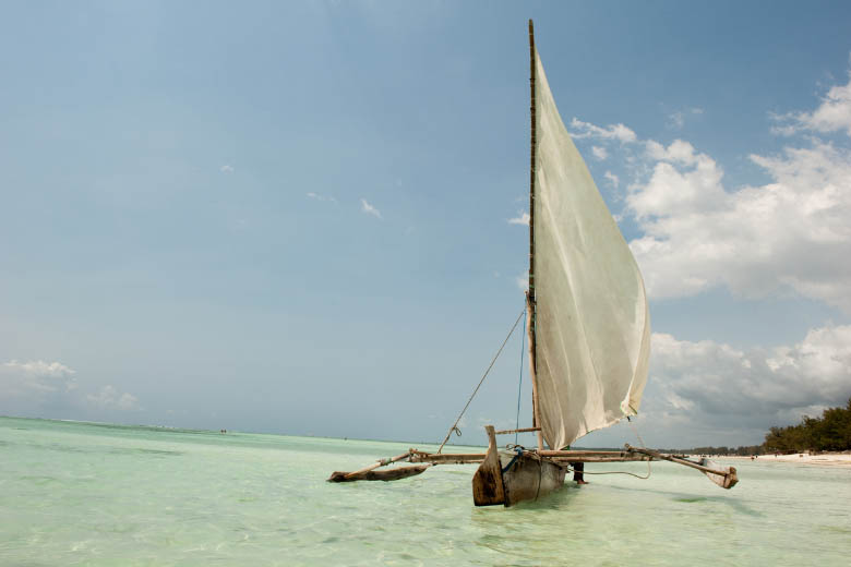 a traditional dhow boat in zanzibar with a white sail floating on crystal clear waters