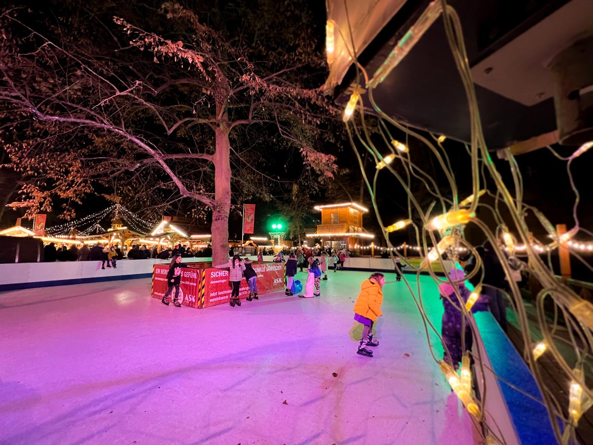 children ice skating on a small ice rink surrounded by fairylights